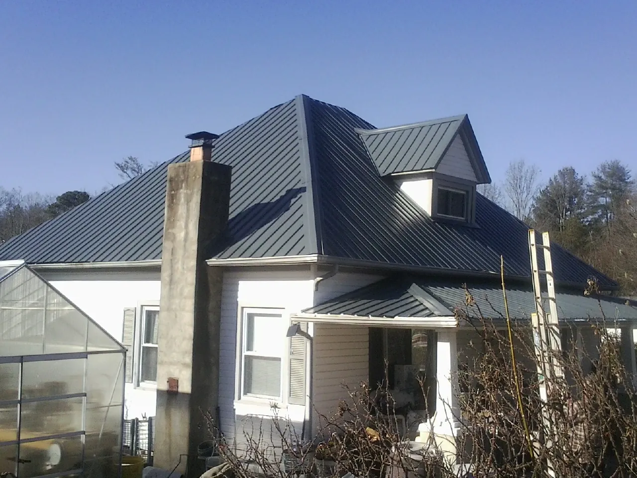 Dark blue standing seam metal roof on a white farmhouse with dormer — Slate & Tile Roof Repair by Roofing Brothers in Geff