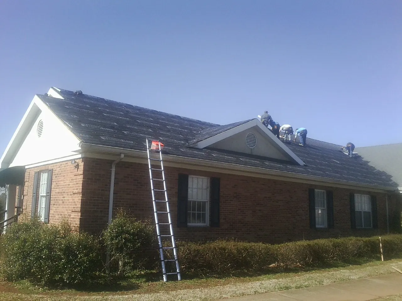Crew tearing shingles off a brick ranch roof with a ladder set — Emergency Roof Repair work by our crew in Geff