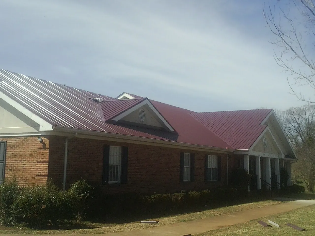 Red metal roof with gabled entries on a long brick building, from a Hail Damage Roof Repair job in Geff
