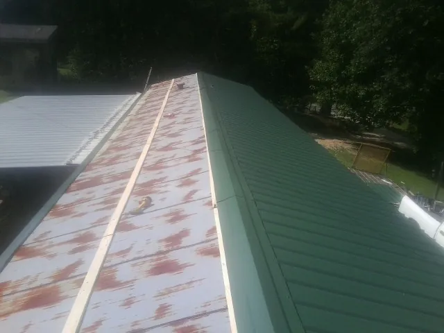 Old rusted panels beside newly installed green metal roofing — Wind Damage Roof Repair by Roofing Brothers in Geff