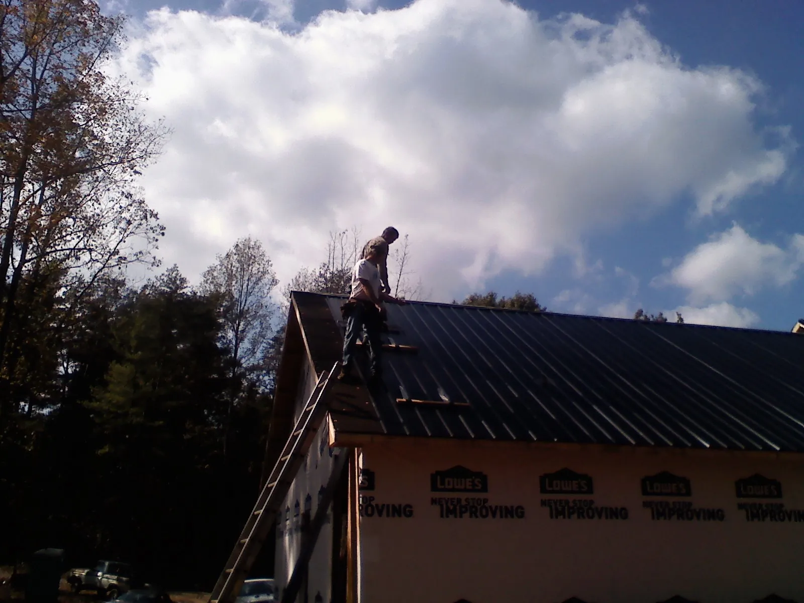 Roofer fastening dark metal panels high against a cloudy sky, from a Roof Inspection job in Geff