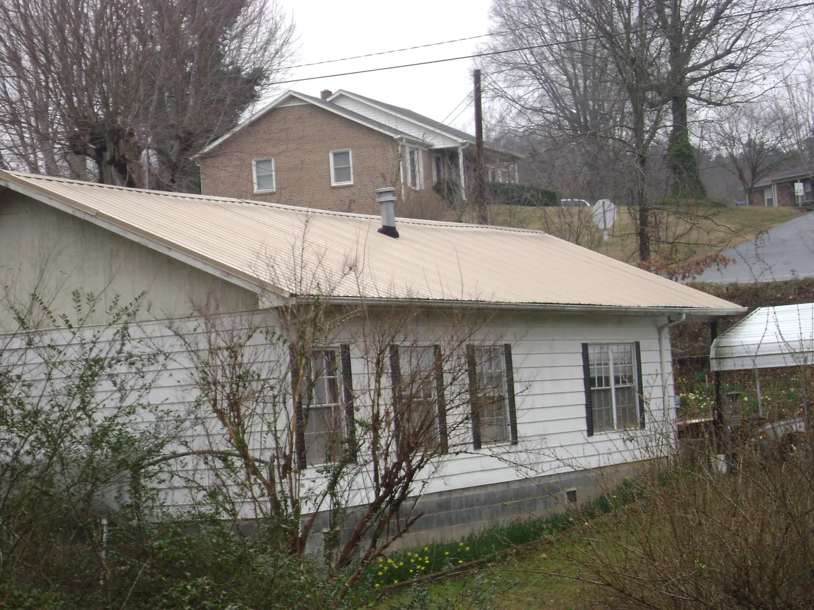 Tan metal roof on a white sided house set into a hillside — Commercial Roofing by Roofing Brothers in Geff